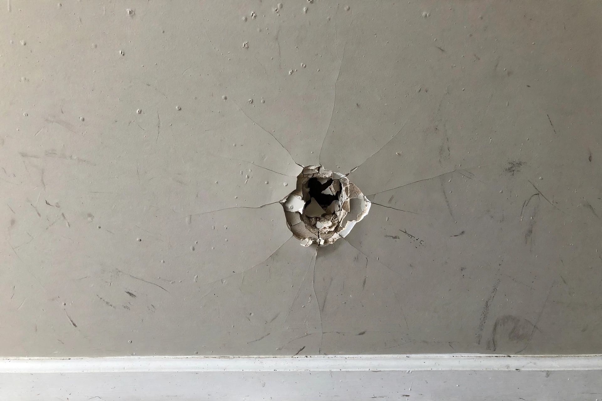 Drywall wall with a doorknob hole, cracks and scuffs before repair